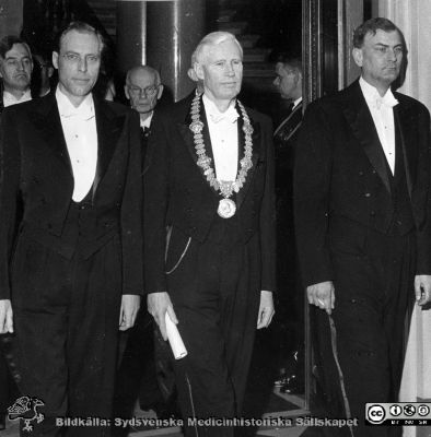 Professorsinstallation 18.4. 1959 
  Rector magn. Prof. Philip Sandblom, flankerad av fr.v.  prof. Hans Ronge (hygien)och prof. Gunnar Lindgren (socialmedicin).
Nyckelord: Professorsinstallation;Rector Magnificus;Lunds universitet;Medicinska fakulteten;Socialmedicin;Hygien