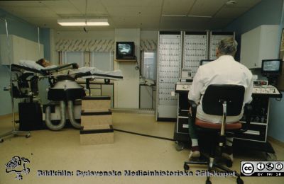 "Stenkrossen" c:a 1979 i Lund, nyinstallerad. 
Sjukhusfotograferna i Lund 1989.  Litotriptor, en apparat för att med ultraljud slå sönder njurstenar. En statist ligger i maskinen. Troligen docent Eric Lindstedt vid manöverpanelen. Se också bild SMHS14552 som visar samma sak i svart-vitt.
Nyckelord: Urologisk;Litotriptor;Litotripsi;Klinik;Universitetssjukhuset i Lund;USiL