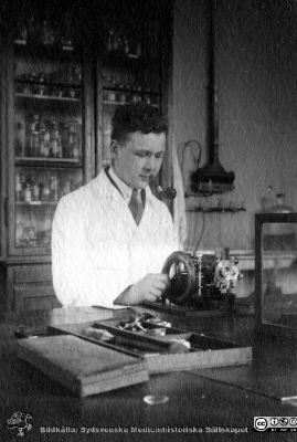Fotoalbum tillägnat Professor Torsten Hellman Från Tacksamma Lärjungar 3.4.1924. 
Fotoalbum tillägnat Professor Torsten Hellman Från Tacksamma Lärjungar 3.4.1924. 
Bildtext: "Peter Varenius". 
Han sitter vid en laboratoriebänk med en mikrotom för att skära snitt att montera på objektsglas för senare färgning.
Nyckelord: Histologiska avdelningen;Anatomiska Institutionen;Medicinska fakulteten i Lund;Locus Medicus Lundensis;Kurslaboration;Universitet