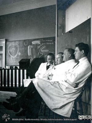 Thesaurus histologiae 1926
Fotoalbum på första bladet märkt 
"Thesaurus histologiae. Det är een obiektiv beskrifning aff hendelser på Den histologiska skåådebanan A.D. MDMXXVI. Med tacksamhet och vördnad överräckt av Kurs och amanuenser." 
Detta album innehåller bilder från histologiska avdelningen 
på anatomiska institutionen i Lund på Biskopsgatan 7. Bildtext Fig 3. Misslyckad stämningsbild. Frän vänster kanske amanuens Sture Siwe, kanske amanuens Gösta Glimstedt, Professor Torsten Hellman och okänd amanuens.
Bildkälla Stiftelsen Locus Medicus Lundensis 250317. Fotograf okänd.
Nyckelord: Anatomiska Institutionen;Histologiska avdelningen;Medicinska fakulteten i Lund;Universitetet;Lärare;Föreläsningsal