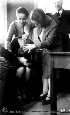 Fotoalbum märkt Histologikursen Ht. -27 på första bladet. 
Fotoalbum märkt Histologikursen Ht. -27 på första bladet. Det innehåller bilder från dåvarande histologiska avdelningen 
på anatomiska institutionen i Lund på Biskopsgatan 7. Bildtext "Kvinnlig fägring", men saknas i övrigt. Bilden visar två studentskor som tycks klippa nackhåret på en tredje. Bordet till höger i bilden antyder att den är tagen i kurslaboratoriet.
Bildkälla Stiftelsen Locus Medicus Lundensis 250317. Fotograf okänd.
Nyckelord: Medicine studerande;Studenter;Anatomiska Institutionen;Histologiska avdelningen;Medicinska fakulteten i Lund;Universitet