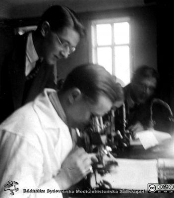 1928 års kurs i histologi i Lund
Fotoalbum märkt Histologikursen anno 1928. 
Detta album innehåller bilder från dåvarande histologiska avdelningen på anatomiska institutionen i Lund på Biskopsgatan 7. Liksom de övriga i serien skapades det av kursdeltagarna och tillägnades kursledaren, professor Torsten Hellman, som uppskattning av hans lärargärning. Bildtext nedanför: "Stig Ahnlund. Dahlin".  Henry Dahlin var amanuens och satt vid mikroskopet.
Bildkälla Stiftelsen Locus Medicus Lundensis 250317.
Nyckelord: Locus Medicus Lundensis;Medicinska fakulteten i Lund;Histologiska avdelningen;Sydsvenska Medicinhistoriska Sällskapet;SMHS;Anatomiska Institutionen;Studenter;Lärare