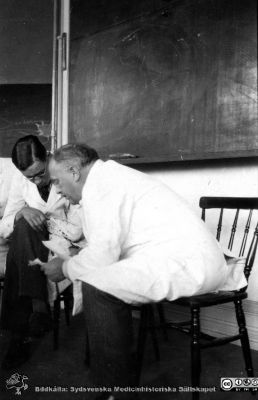 Foton från histologkursen i Lund 1929. 
Fotoalbum tillägnat Professor Torsten Hellman med tacksamhet och vördnad från histologkursen 1929. "Chefen", Torsten Hellman, i en pinnstol framför svarta tavlan i föreläsningssalen tillsammans med en amanuens?
Nyckelord: Anatomiska Institutionen;Histologiska avdelningen;Föreläsningssal;Medicinska fakulteten i Lund;Medicinska fakulteten i Lund;Universitet;Locus Medicus Lundensis