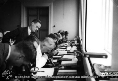 Fotoalbum "Kursen i histologi H T 1932.
Fotoalbum "Kursen i histologi H T 1932".  Bildtext saknas. Bilden visar professor Torsten Hellman i ljus laboratorierock vid mikroskopet tillsamans med medicine studerande i histologiska avdelningens mikroskoperingssal på anatomiska institutionen i Lund. 
Bildkälla stiftelsen Locus Medicus Lundensis och Sydsvenska Medicinhistoriska Sällskapet / SMHS. Fotograf okänd.
Nyckelord: Medicine studerande;Histologiska avdelningen;Anatomiska Institutionen;Medicinska fakulteten i Lund;Locus Medicus Lundensis;Universitetet i Lund