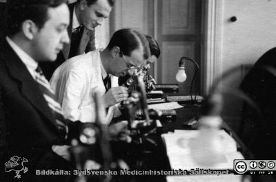 Fotoalbum  tillägnat Professor Torsten Hellman av lärjungarna 1935. Bildtext saknas. En kursamanuens hjälper studenterna med mikroskopering. De är medicine studerande på avdelningen för histologi på anatomiska institutionen i Lund. 
Bildkälla stiftelsen Locus Medicus Lundensis och Sydsvenska Medicinhistoriska Sällskapet / SMHS. Fotograf okänd.
Nyckelord: Histologiska avdelningen;Anatomiska Institutionen;Sydsvenska Medicinhistoriska Sällskapet;Medicinska fakulteten i Lund;Locus Medicus Lundensis;Medicine studerande;Lunds universitet