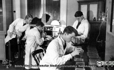 Fotoalbum  tillägnat Professor Torsten Hellman av lärjungarna 1935. Bildtext: Laborationer. Preparaten färgas". Fyra unga medicinare i kurslaboratoriet. De är medicine studerande på avdelningen för histologi på anatomiska institutionen i Lund. 
Bildkälla stiftelsen Locus Medicus Lundensis och Sydsvenska Medicinhistoriska Sällskapet / SMHS. Fotograf okänd.
Nyckelord: Histologiska avdelningen;Anatomiska Institutionen;Sydsvenska Medicinhistoriska Sällskapet;Medicinska fakulteten i Lund;Locus Medicus Lundensis;Medicine studerande;Lunds universitet;Kurslaboratorium