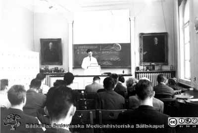 Docent Unne Stenram föreläser på patologiska Institutionen
Docent Unne Stenram föreläser  om glomerulonefrit och njursjukdomar på patologiska institutionen i Lund någon gång i slutet av 1950 -talet, senast 1962. På fondväggen till vänster en oljemålning av Einar Sjövall och till höger av John Forssman. Båda var professorer i patologi i Lund. Unne Stenram blev så småningom också professor i patologi i Lund.
Nyckelord: Lasarett;Lund;Universitet;Universitetssjukhus;USiL;Utbildning;Kurs;Kandidat;Patologi;Föreläsning