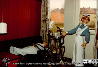 En s.k. Lundiarespirator på en utställning om respiratorvård vid 100-årsjubileet för infektionskliniken i Malmö 1980
Utställningen stod i anslutning till sjukhusets personalmatsal. Apparaten är en Lundiarespirator som utprovades på 1950-talet på kliniken. På "patienten" sitter ett s.k. Jacksonbälte som tryckte ihop bröstkorgen för att hjälpa patienten med utandning. Sköterskans uniform är typisk för 1950-talets lundautbildade SSSH-sköterskor, med mössa och hakband. Bildkälla Klas Ramnerö 2014.
Nyckelord: UMAS;MAS;Malmö_;Allmänna;Sjukhus;Epidemi;Infektion;Andning;Andningsvård;Respirator;Utställning;Jubileum