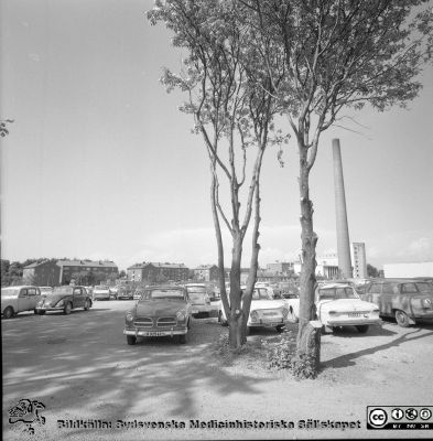 Vy mot sköterskebostäderna och panncetnralen från centralblockets norrsida
Sjukhusfotograferna i Lund. Pärm Diverse tagningar. 1971, 1972, 1973. Exteriörer, lasarettsområdet juli 1971.  Från negativ.
Nyckelord: Lund;Lasarett;Universitet;Universitetssjukhus;USiL;Panncentral;Bostad;Sjuksköterska;Parkering