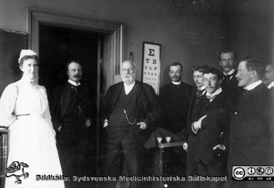 Prof Michael Kolmodin Löwegren i sin klinik år 1903
Från vänster översköterskan Klara T. Löwenadler. dåvarande docenten, sedermera professorn i oftalmiatrik Albin Dalén, t. h. tjänstgörande vid kliniken Gustaf Pallin, Emil Westergård, Herold Hirschlaff, Herman Wallengren och Sven Johansson. 
Fotografi från Mikaël K. Löwegrens efterlämnade handlingar. Samma bild som 030205c. Bildkälla: M.K. Löwegrens efterlämnade handlingar hos Aino Milner i Dalby 2013, från 2015 på UB i Luind. 
Nyckelord: Lasarett;Lund;Universitetssjukhus;USiL;Ögon;Klinik;Oftalmologi