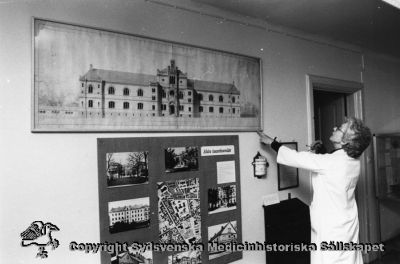 Medicinhistorisk utställning i seminariets bottenvåning nov. 1986. 
Agnete Bisgaard justerar hängningen av Helgo Zettervall teckning av kirurgiska kliniken i Lund av år 1867. Foto Ernst von Scheele.
Nyckelord: Universitetssjukhus;Utställning;Lund;Medicinhistoriskt;Museum;Helgo;Zettervall;Skärm;Agnete;Bisgaard;Foto;Omonterat;Ernst;von Scheele;Kapsel 07