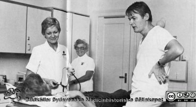 Dr Sverker Hellsten och syster Birgitta Tilly på urologmottaningen i Malmö år 1975.
 I bakgrunden undersköterskan Margit Jönsson. Bildkälla: Sverker Hellsten.
Nyckelord: UMAS;MAS;Malmö_;Allmänna;Sjukhus;Urologi;Mottagning