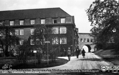 Fotografiskt vykort med dåvarande medicinska kliniken vid lasarettert i Lund
Vy mot norr. Foto rimligen i mitten på 1900-talet, efter tillkomsten av valvet över till reumatologiska kliniken  på 1920-talet och före 1968 då lasarettets centralblock stod klart. Från repronegativ i lasarettsfotografernas pärm "Gammalt A". Lund. 
Nyckelord: Lund; Lasarett; Exteriör; Vykort; Universitet; Universitetssjukhus; Medicin; Intern; Klinik