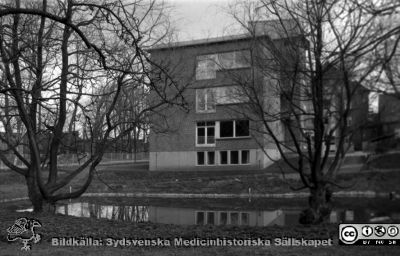 Reumatologiska klinikens östra gavel. 
Husets sockel och markens utseende mellan denna och dammen antyder att huset är alldles nybyggt. Från 35 mm repronegativ i lasarettsfotograferna i Lunds arkiv. Pärm "Gammalt A".
Nyckelord: Lasarettet;Lund;Universitet;Universitetssjukhuset;Reumatologi;Damm;Märgelgrav