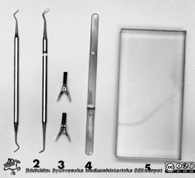 Instrumentsats för uppdukning på centraltandpolikliniken 1969
Pärm "USiL div. tagningar. 1960 och t.v." Centraltandpol. 22/10, 1969. Tandl. Dahl, instrumentdukn. Från negativ.
1. Kulstoppare liten
2. Silikatinstrument
3. Stripsklämmor
4. Silikatspatel
5. Silikatglasplatta
Nyckelord: Lund;Lasarett;Universitet;Universitetssjukhus;Dental;Klinik;Oral;Kirurgi;Instrument