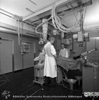 Docenten (senare professorn) Erik Boijsen med röntgensköterskan Kerstin Ahldin i ett angiografirum i Lund 1969
Pärm USiL div. tagningar 1960 och t.v. Angiolab RTG 1/9 1969. Från negativ. Erik Boijsen och röntgensköterskan Kerstin Ahldin.
Nyckelord: Lund;Lasarett;Universitet;Universitetssjukhus;Röntgen;Kärl;Angiografi;Rtg