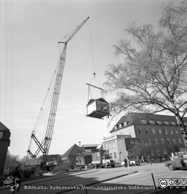 Forskningsbaracken på innergården i den tidigare medicinska kliniken tas bort
Pärm "USiL div. tagningar. 1960 och t.v.". Foto 1968. Från negativ. - Bildserien visar rimligen borttagningen av den barack med forskningsutrymmen som något decennium tidigare hade satts på en av mediciniska klinikens innergårdar. Medicinska klinkiken hade 1968 flyttat in i det nya centralblocket, vilket nog var varför baracken togs bort.
Nyckelord: Lund;Lasarett;Sjukhus;Universitet;Universitetssjukhus;Intern;Medicin;Klinik;Forskning;Barack