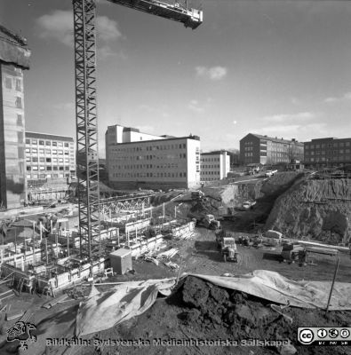 Cetralblocket i Lund byggs 1965
Pärm "Div. tagningar 1960 och t.v.". Mars 1965. Centralblocket på Lasarettet i Lund har just börjat byggas. Till vänster i bakgrunden skymtar det tidigare byggda AB-blocket. Strax hitom ett glidformsgjutet betongtorn för det norra hissbatteriet. I bildens mitt E-blockets redan byggda första flyglar. I bakgrunden till höger om dessa psykiatriska och barnpsykiatdriska klinikerna. I förgrunden läggs grunden för det södra hissbatteriets torn och D-flyglarna. Från negativ.
Nyckelord: Lund;Lasarett;Universitet;Universitetssjukhus;Centralblocket;USiL;Bygge;Grundläggning;Hissbatteri;Torn