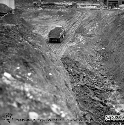 Cetralblocket i Lund byggs 1964
Pärm "Div. tagningar 1960 och t.v.". Foto 1964. Blocket grävdes ned två våningar mer än ursprungligen planerat. Det blev en djup grop. I bakgrunden skymtar ingången till dåvadrande barnpsykiatriska kliniken (från 1986 Ögon B). Från negativ.
Nyckelord: Lund;Lasarett;Universitet;Universitetssjukhus;Centralblocket;USiL;Bygge