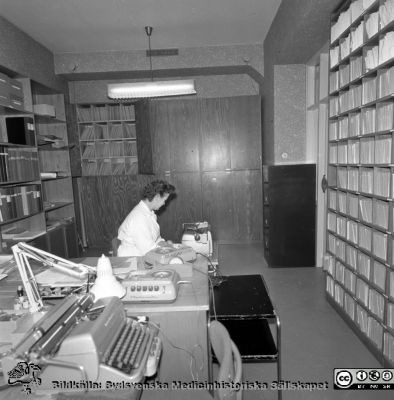 Lasarettet i Lund år 1967. Öronklinikens expedition.
Lasarettsfotograferna. Lund. Pärm "Div. tagningar, 1960 och t.v.". Foto 1967. Sekreterare på öronklinikens skrivexpedition och journalarkiv. Sekreteraren har inte identifierats. Från negativ
Nyckelord: Lund;Lasarett;Universitet;Universitetssjukhus;USiL;Öron;ÖNH;Öron-näsa-hals;Otologi;Otiatri;Administration;Sekreterare;Expedition