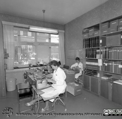 Lasarettet i Lund år 1967. Öronklinikens expedition.
Lasarettsfotograferna. Lund. Pärm "Div. tagningar, 1960 och t.v.". Foto 1967. Skrivexpedition och journalarkiv på öronkliniken. Personerna i bilden har inte identifierats. Från negativ.
Nyckelord: Lund;Lasarett;Universitet;Universitetssjukhus;USiL;Öron;ÖNH;Öron-näsa-hals;Otologi;Otiatri;Administration;Sekreterare;Expedition