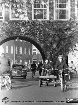 Höstlig vy 1961 med cykel- och biltrafik under valvet mellan medicinska (till vänster) och reumatologiska (till höger) klinikerna. 
Lasarettsfotograferna. Lund. Pärm "Div. tagningar, 1960 och t.v.". Lasarettets exteriörer, 1960-talet. Foto 1961. Från negativ
Nyckelord: Lasarett;Lund;Universitet;Universitetssjukhus;USiL;Medicin;Reumatologi;Valv;Cyklist;Trafik