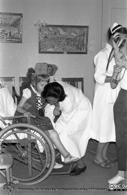 Julhälsning 1962 från barnavdelningen på reumatologiska kliniken
Lasarettsfotograferna. Lund. Pärm "Div. tagningar, 1960 och t.v.". Reumaten, barn, till "julhälsning", 1962. Kenske dr Helena Svantesson f. Zymler som hjälper flickan i rullstol. Notera flickans svullna leder i benet. Från negativ. 
Nyckelord: Lasarett;Lund;Universitet;Universitetssjukhus;USiL;Reumatologi;Klinik;Julhälsning