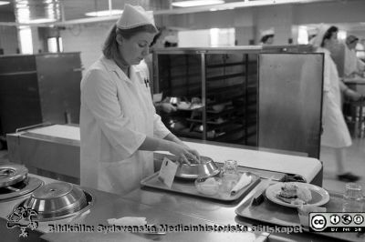 Brickdukning vid löpande band i centralköket
Sjukhusfotograferna i Lund. Pärm negativ, 1979:1. 46. 79-05-04. Från negativ
Nyckelord: Lasarettet;Lund;Universitetssjukhus;USiL;Centralkök;Distribution;Patientmat;Brickdukning