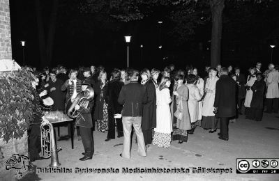 Neurokirurgisk fest 1976
Sjukhusfotograferna i Lund. Pärm Negativ, S/V. 1976.	145. Neurokirurgisk fest 8/10-76 när de båda neurokirurgiska klinikerna A och B slogs samman till en. Orkestern Corps Callosum kopplar av efter konserten utanför gamla kirurgen där plaketten satts upp. Man ser Göran Sundbärg med bastuban, Erik Kågström och längst tv Bengt Sjölund. Stig Rehncrona skymtar bortom honom, med mörka glasögon och virveltrumma. Längst ut till höger syns vår sudanesiske medarbetare Ali Abdul Rahman doktorand och under specialistutbildning hos oss. Från negativ.
Nyckelord: Lasarett;Lund;Universitet;Universitetssjukhus;USiL;Neurokirurgi;Fest