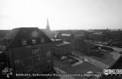 Vy söderut i motljus från radiologiska klinikens tak.
Sjukhusfotograferna i Lund. Pärm Negativ, S/V. 1976. 32.  Notera "solkatterna" på fr.a. öronklinikens fasad; reflexer från radiologiska klinikens eller kanske centralblockets fönster. 
Till vänster öronklinikens första byggnad från 1930-talet. Strax till höger om den deras annex från 1950-talet. Ytterligare till höger 1918 års panncentral, nu med den stora skorstenen riven och viss tillbyggnad. Till höger infektionsklinikens nya och gamla byggnader. Allhelgonakyrkan i bakgrunden. Från negativ. 
Nyckelord: Lasarettet;Lund;Universitet;Universitetssjukhus;USiL;ÖNH;Öron-Näsa-Hals;Oto-rino-laryngologi;MTA;Maskin;Panncentral;Infektion;Epidemi;Klinik