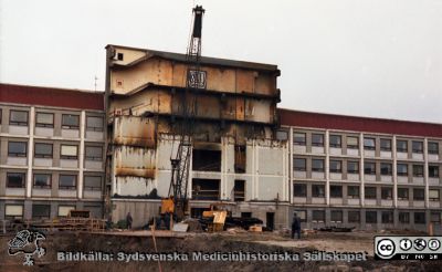 Fasadarbete och grävning för centralblocket
Pärm Lasarettsfoto, interiörer och exteriörer m.m. 1958 - 1960. Med stora svetslågor har man skurit loss den södra fasaden från AB-blockets trapphus, och här lyfts den ned, bit för bit. Här skall C-blocket ansluta. Foto 1960. Från negativ. 
Nyckelord: Lund;Lasarett;Universitet;Universitetssjukhus;USiL;Blocket;Bygge;Grävning