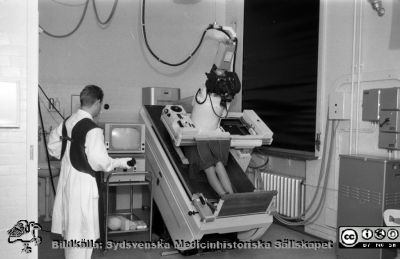  Lunds första röntgenapparat med bildförstärkare och TV-länk
Pärm Lasarettsfoto, interiörer och exteriörer m.m. 1958 - 1960. 15. Rtg. I. 1960. Samma fotorillfälle som bild 101114-059. Philipstillverkad apparat med modifikationer av Henry Wallman, som var en av pionjärerna när det gäller bildförstärkare med TV-länk. Apparaturen användes för magsäckar, matstrupe, flebografi, pacemakerinläggningar, främmande kroppar i lungor. Operatören kan kanske vara Jan Nilsson, senare överläkare i Helsingborg. Foto för en bok om röntgenteknik som utgavs av Kodak. Från negativ. 
Nyckelord: Lasarettet;Lund;Universitet;Universitetssjukhus;USiL;Rtg;Röntgen;Radiologi