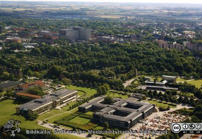 Lasarettet i Lund och landstingshuset på Baravägen i Lund. 
Sjukhusfotograferna i Lund. Plast-ficka, lösa bilder, 1980-90-talen.	Foto på 1990-talet, efter 1993 (då strålbehandlingavdelningen stod klar) men före barnkliniken BUS och BMC börjat byggas, dvs före 1998. F-blocket har byggts. Det ovala parkeringshuset närmast folkskoleseminariet är under byggnad. Från originalfoto
Nyckelord: Lasarett;Lund;Universitet;Blocket;Flygfoto;Lundsting;Malmöhus;Läns;Baravägen