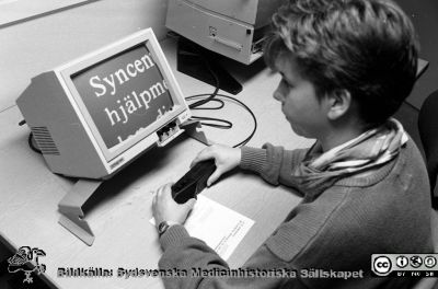 Syncentralen i Lund. 
Sjukhusfotograferna i Lund. Pärm Negativ, Dia, 1987. 50/1987. A. 87-04-06. Syncentralen i Lund. Synpedagog Pia Daag demonstrer lästeknik vid en dators bildskärm och med en kamera i hanen; osedvanligt liten för att vara från den tiden. Från negativ.
Nyckelord: Lasarettet;Lund;Universitetssjukhus;USiL;Ögon;Syncentral;Oftalmologi;Handikapp;Synskadad;Synhjälp