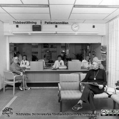 Stora väntrummet på nya Ögonkliniken B i Lund 1987
Sjukhusfotograferna i Lund. Pärm Negativ, Dia, 1987. 94/87. Det var också trapphall. Sekreterarna vid disken är NN, Gun (Olsson?) och Katarina Ryd. De väntande patienterna hade medgett fotografering och publicering. Från negativ. 
