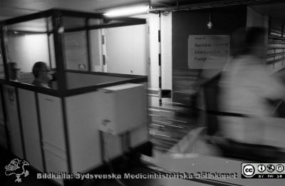 Patienttransport i kulverten med elektrisk truck och "passagerarvagn" 1987 
Sjukhusfotograferna i Lund. Pärm Svart-vita neg. 1987. 87-09-29. Från negativ.
Nyckelord: Lasarettet;Lund;Universitetssjukhus;USiL;Patient;Transport;Kulvert;Tåg