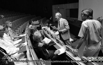 Administrativa chefer inför ett möte i aulan på Centralblocket i Lun
Sjukhusfotograferna i Lund. Pärm Svart-vita neg. 1987. 105/-87. 87-08-24.  Stående sjukhusdirektör Kurt Roos och biträdande dito Ingvar Wiberg. Bland de sittande syns bl.a Bengt Löw, Thomas White och Mark Blomberg. Från negativ. 
Nyckelord: Lasarettet;Lund;Universitetssjukhus;USiL;Administration;Chefer;Möte