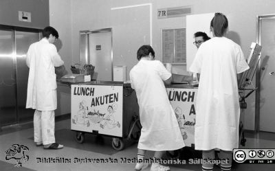 Lunchakuten 1991
Pärm  Lasarettsfotograferna i Lund, negativ, 1991. 7. 91-02-27. A.O.65. "Lunchakuten", vagnar med färdiglagad mat i portionslådor i hisshallen på ett av de övre planen i centralblocket. Fram till våren 2015 sköttes personalmaten på entreprenad av firma Medirest. Från negativ. 
Nyckelord: Lasarettet;Lund;Medirest;Universitetssjukhuset;USiL;Mat;Servering