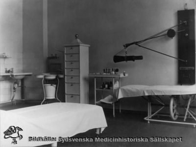 Ögonkliniken i Lund på södra lasarettsområdet i mitten på 1920-talet
Operations- eller behandlingsrum på ögonkliniken i Lund i mitten på 1920-talet. Till höger invid väggen ett höj- och sänkbart operationsbord. Till vänster ett ställ med en spann och handfat tvagnings- och sköljfat av den typ som användes vid denna tid, liksom tvättställ på väggen med rinnande vatten. 
Foto Alfr. Hagblom, Lund för ett fotoalbum tillägnat professor Gustaf Ahlström när han pensionerades år 1927.
Nyckelord: Ögon;Ögonklinik;Oftalmologi;Oftalmiatrik;Lund;Lasarett;Södra;Område;
