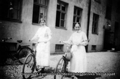 Syster Dera och syster Elida på cykelrond på Vipeholms sjukhus.
Vipeholm personal. Etikett: PÅ CYKELROND. Till vänster syster Dera. Till höger syster Elida. Publicerad på sid 86 i Carlén-Nilsson C, Holmér U (1998) Röster från Vipeholm. pp. 1-127 Stiftelsen medicinhistoriska museerna i Lund och Helsingborg, Lund. Foto Omonterat
- Sköterskorna har hakband, dvs de är färdigutbildade. Foto rimligen i mitten på 1900-talet.
Nyckelord: Syster;Sköterska;Cykel;Cykelrond;Dera;Elida;Hakband;Foto;Omonterat;Kapsel 16