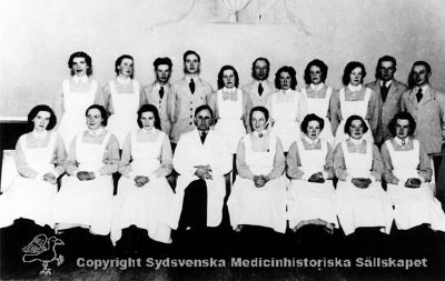 Elevkurs på Vipeholms sjukhus 1938-1939
Vipeholm utbildn. personal. Elevkurs. Praktiska delen avslutad den 21 / 10 1938, Teoretiska delen avslutad den 9 / 3 1939. Övre raden från vänster: Astrid Teresia Pettersson, Herta Linnea Bengtsson, Sten Ingvar Pettersson, Henning Rudolf Axelsson, Margit Berta Ingegärd Gustavsson, Ove Cristian Scharffenberg, Rut Signe Bohman, Rut Ingeborg Erlandsson, Signe Viola Dahlman, Hans Åke Andersson, Henry Gerhard Friman. Nedre raden från vänster: Hulda Märta Linnea Eliasson, Rut Signe Ekdahl, Marta Elisabet Ohlsson, Överläkare Hugo Fröderberg, Förestånderskan Elida Nilsson, Vera Gulli Ohlsson, Hilda Augusta Malmqvist, Elna Elisabet Andersson.  	Foto	Omonterat
Nyckelord: Vipeholm;Utbildning;Personal;Kapsel 16;Foto;Omonterat;1938;1939