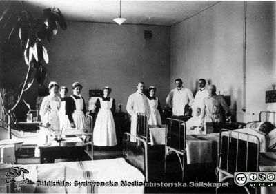 Professor Ribbing på rond i gamla medicinska kliniken år 1910
Ur pärm med bilder tänkta för A. Flaum "Lasarettet i Lund" (1968). Nu finns elektrisk belysning och värmeledning.Kaminer och kakelugnar togs bort här år1904. Avdelningssköterskan Laura Pedersen utexaminerades med den första SSSH kursen år 1905. Märk de svarta sängtavlorna, påskrivna med krita. Foto, tillhörigt Södra Sveriges Sjuksköterskehem. (Sid.199)
Nyckelord: Lasarettet;Lund;Universitetssjukhuset;USiL;Medicinsk;Klinik;Internmedicinsk