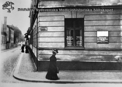 Kurhuset av år 1824, det äldsta kvarvarande hus som tillhört Lasarettet i Lund
Ursprungligen olika polikliniker. Hudklinik i mitten på 1900-talet, senare medicinska fakultetens expedition. Tillhör sedan 1970-talet universitetet. 
Foto rimligen i slutet på 1800-talet, att döma av damernas klädsel.
Nyckelord: Lund;Lasarett;Kurhus;Paradisgatan;Sandgatan;Poliklinik;Dermatologi;Hud;Expedition;Fakultet;Medicin