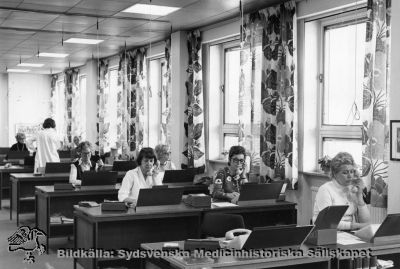 Telefonväxeln på Lasarettet i Lund 16/5 1975.
Påskrift: På lasarettets telefonväxel arbetar 16 heltidsansällda telefonister, 6 vikarier samt en förestånderska. Man expedierar där 8500 inkommande samtal om dagen samt ca 3-400 utgående rikssamtal. Inom sjukhuset finns 1500 anknytningar. (MS-8474).  - Foto monterat på kartong.
Nyckelord: Kapsel 02;Regionarkivet;Lasarettet;Lund;Telefonväxeln;Telefoni;Växel