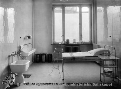 Förlossningsrum på kvinnokliniken i Lund, 1920-talet
Foto Per Bagge, Lund. Man anar Allhelgonakyrkan utanför fönstret, dvs rummet vetter västerut och ligger några våningar upp i sitt hus.
Kvinnokliniken på norra lasarettsområdet togs i bruk 1918, och samma typ av förlossningsbrits, handfat och barnbadkar finns avbildade i Borelius 1918. - Fotografi "från tiden".
Nyckelord: Kapsel 02;Regionarkivet;Lasarettet;Lund;Kvinnokliniken;Förlossningsrum