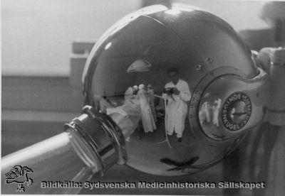 Fotografen speglad i operationsrummets röntgenkula, kirurgiska kliniken i Lund 1937
Påskrift: "Kir. Op. mars 1937. Foto Åke Rydén. LL:s-område söder, interiör. Omonterat foto.
Nyckelord: Kapsel 02;Regionarkivet;Lasarettet;Lund;Kirurgi;Kirurgisk;Klinik;1937;Åke;Rydén