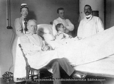 Prof. Seved Ribbing i Lund, sittande vid en sjuksäng 1910
Påskrift på baksidan: "1910. Lasarettsområdet söder." Notera kakelungnen i bakgrunden. Sofiasystern bör vara Inez Oom och läkaren längst till höger Emil Lundström.
Seved Ribbing, född 17 februari 1845 i Stockholm, död 14 februari 1921 i Lund. Medicine doktor 1871, 1872 lasarettsläkare i Simrishamn 1879 e.o. professor i pediatrik och 1888 till professor i praktisk medicin vid Lunds universitet, pensionerad 1910. Åren 1904-07 var han universitetets rektor. - Foto monterat på kartong.
Nyckelord: Kapsel 02;Regionarkivet;Lasarettet;Lund;Medicin;Klinik;Seved;Ribbing;