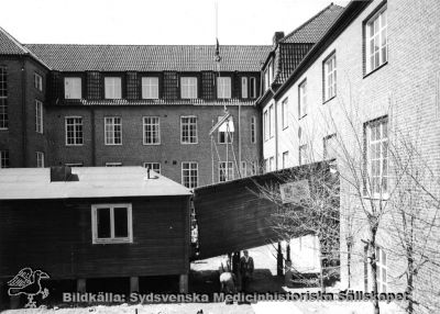 En barack lyfts i delar ut ur en av medicinklinikens innergårdar
En barack för ett forskningslaboratorium lyfts ut ur en av innergårdarna på dåvarande medicinska klinikens byggnad 1968. Fotografi monterat på styv kartong.
Baracken hade byggts i mitten på 1900-talet. Enligt uppgifter framkomna 2014 skall bilderna från baracklyftandet ha tagits 1968, samma år som medicinska kliniken flyttade in i centralblocket. Rimligen visar bildserien alltså hur baracken togs bort. Fil SMHS12297 kommer från samma negativ.
Nyckelord: Kapsel 03;Regionarkivet;Lasarettet;Lund;Medicin;Klinik;Barack;Forskning;Laboratorium