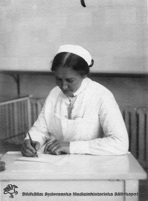 Kanske en barnsköterska i Lund från 1900-talets första halva.
Påskrift: "Personal LL". Omonterat foto utan annan indexeringshjälp. Uniformen och broschen skulle kunna vara en barnsköterskas. Notera bläckhornet och att pennan är av stålfjädertyp, att doppas i bläckhornet. Uniformen, frisyren och andra attribut antyder att bilden är tagen under 1900-talets första halva.
Nyckelord: Kapsel 04;Personal;Foto;Omonterat;Bläckhorn;Stålfjäderpenna