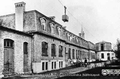 Ekonomibyggnaden vid Lasarettet i Lund från 1904
Man ser mattransportvagnen på linbanan. Vid lasarettets häst och vagn för transporter står syssloman P. Lundborg. Foto i Lasarettsarkivet. Publicerad i Flaum 1968 Sid. 193.
Nyckelord: Kapsel 17;Lasarettet;Lund;Södra;Ekonomi;Ekonomibyggnad;Tvätt;Kök;Linbana;Syssloman;Lundborg